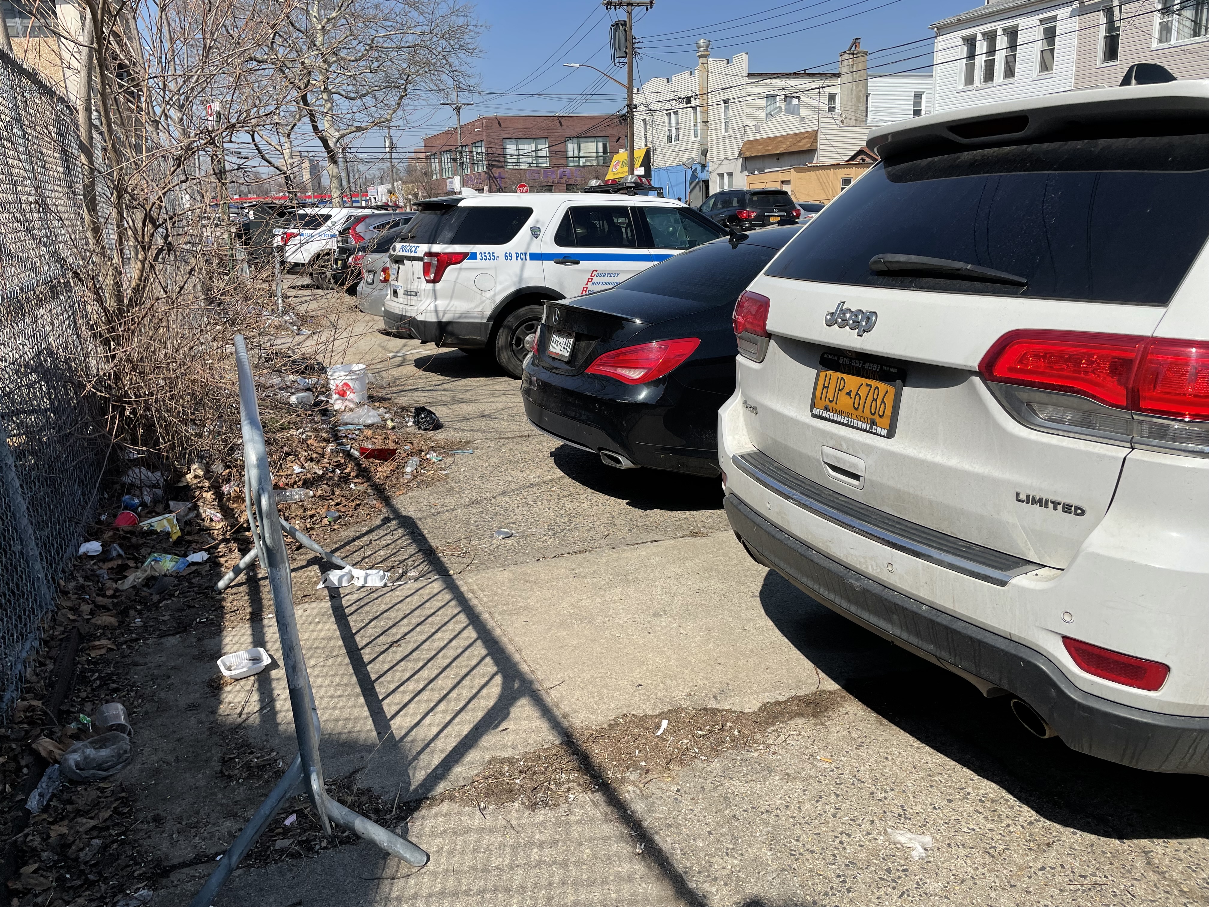 Most of the sidewalk cut off by cars parked outside the 69th Precinct.