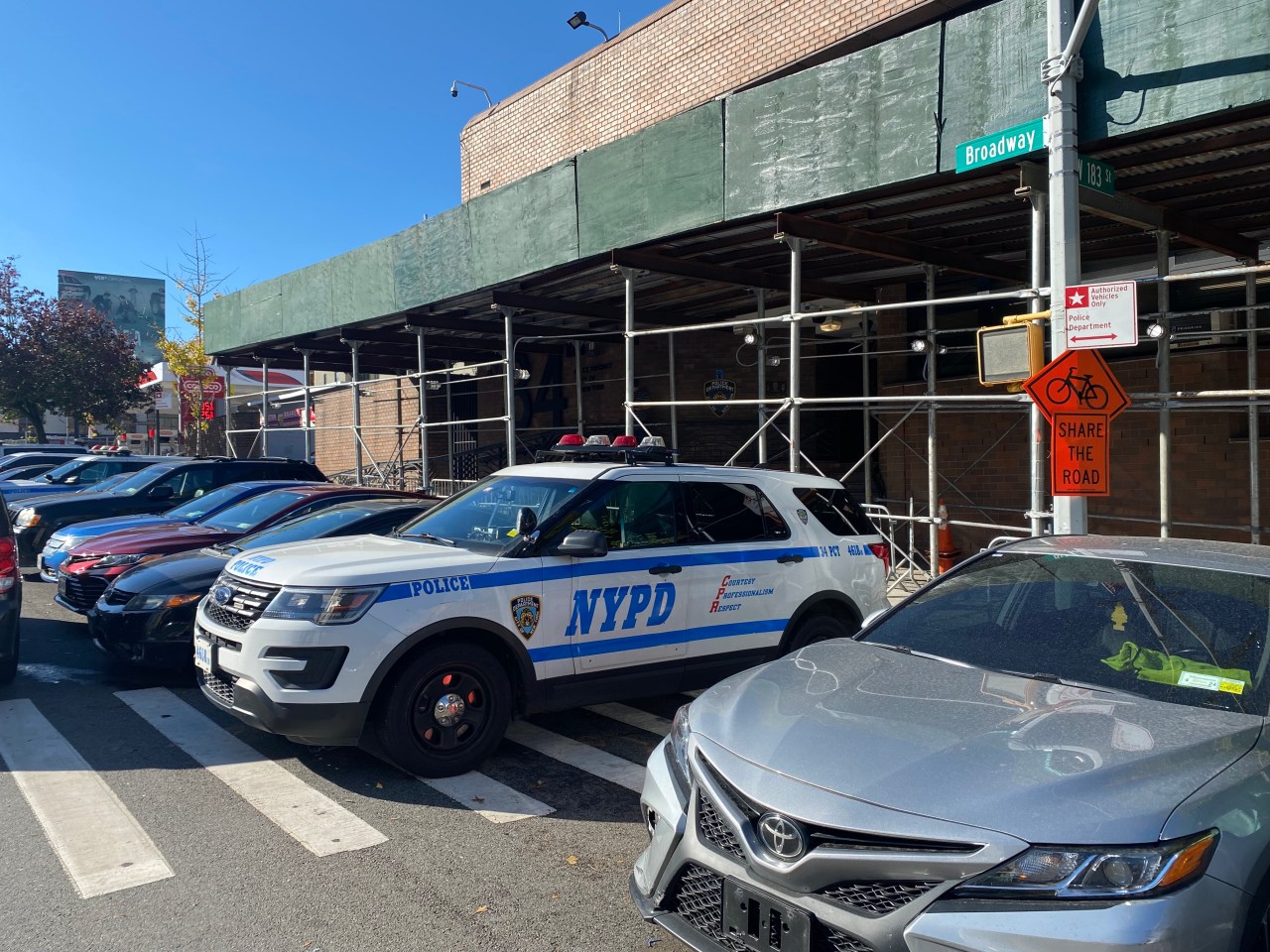 A cop car blocks the sidewalk outside the 34th Police Precinct. The vehicle next to it is missing its front plate. Photo: Kevin Duggan
